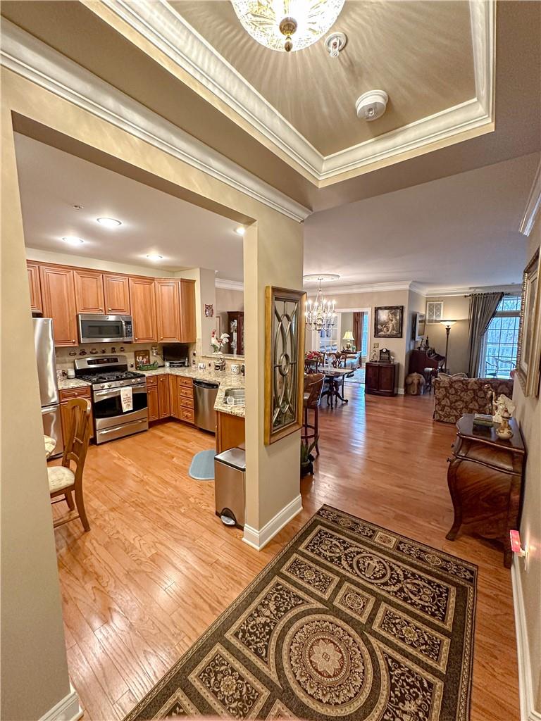 Kitchen featuring a tray ceiling, crown molding, stainless steel appliances, light wood flooring, and a chandelier
