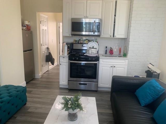 Open concept, light wood-type flooring, living area, kitchen with white cabinetry, stainless steel appliances, and tasteful backsplash