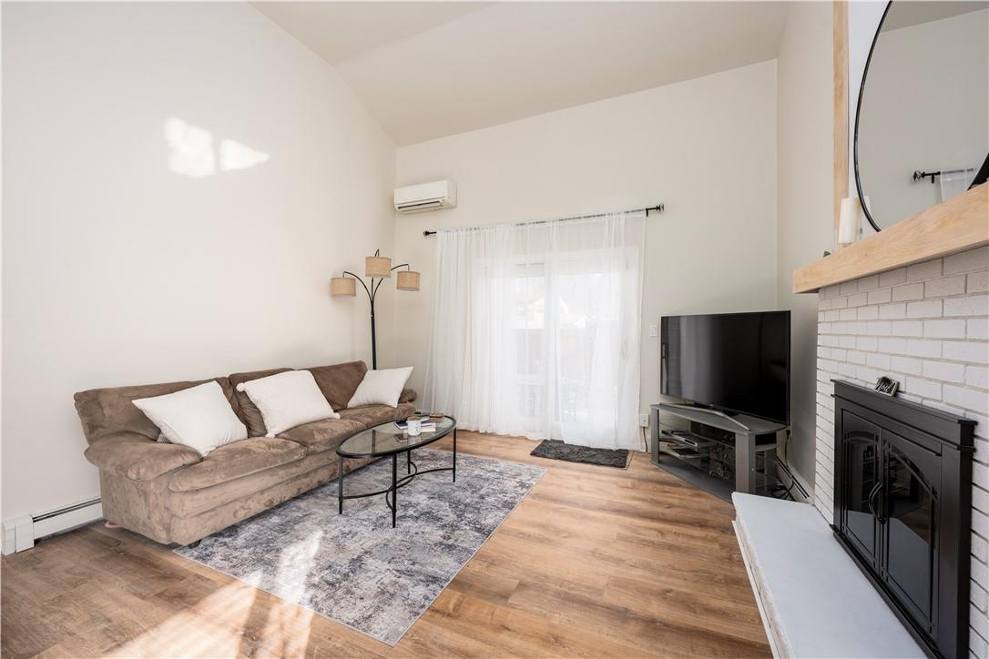Living room with a fireplace, hardwood / wood-style floors, a wall mounted air conditioner, lofted ceiling, and a baseboard radiator