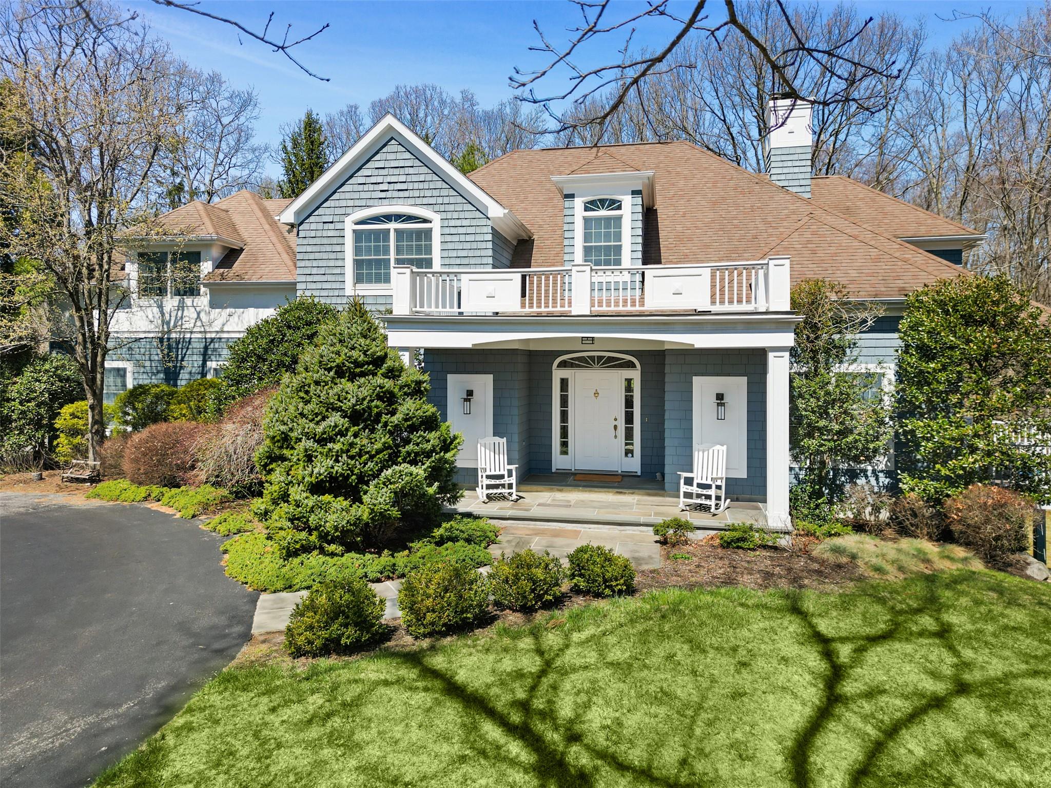 View of front of house featuring covered porch, a front lawn, a balcony, a chimney, and a shingled roof