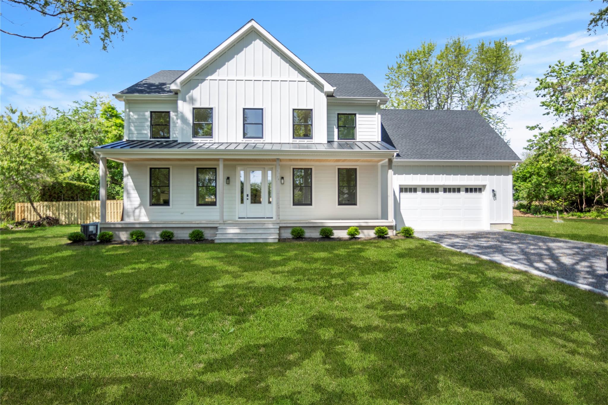 Modern farmhouse style home with a standing seam roof, an attached garage, covered porch, driveway, and board and batten siding