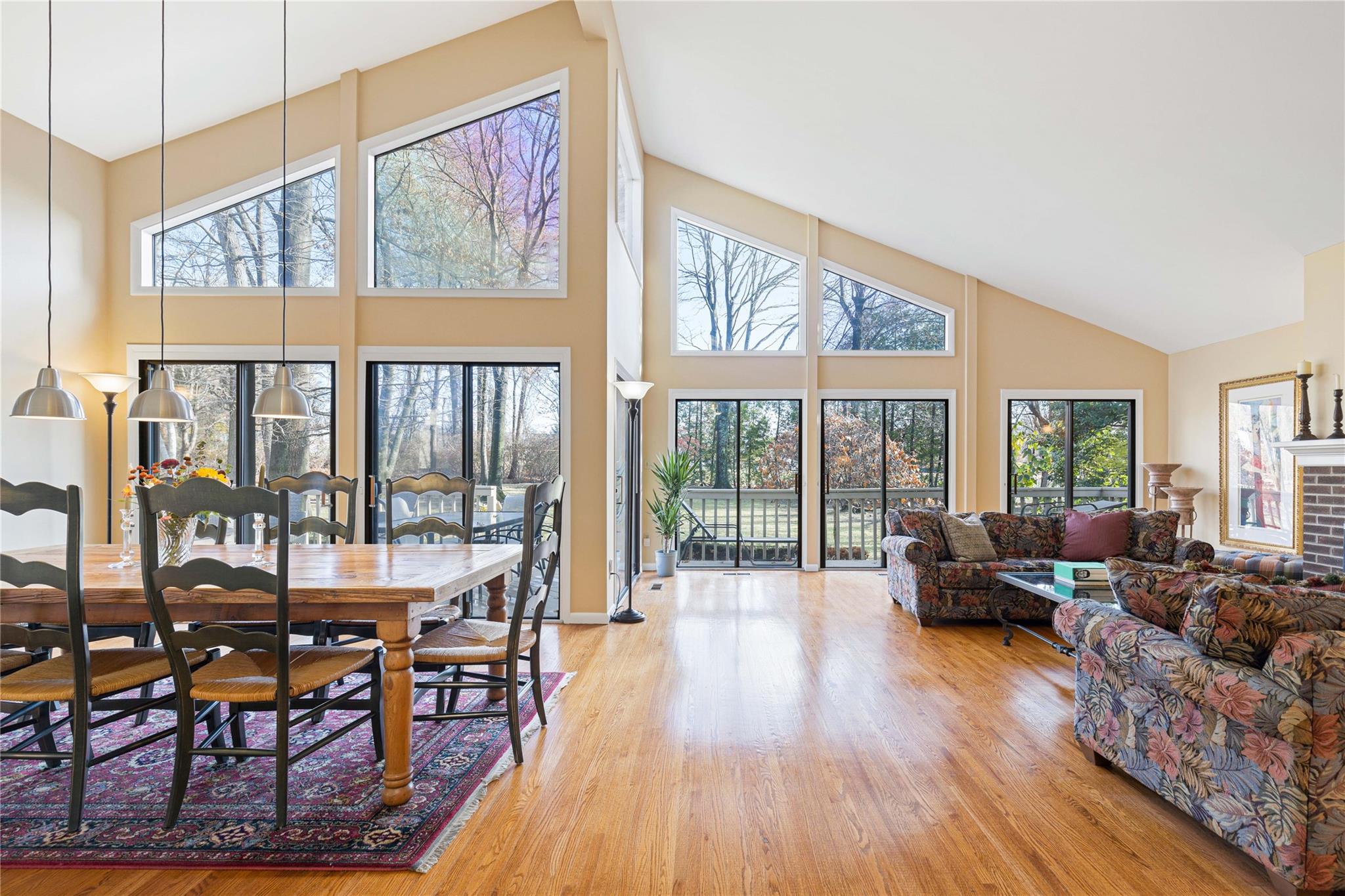 Dining room with wood-flooring, a brick fireplace, high vaulted ceiling, and a healthy amount of sunlight