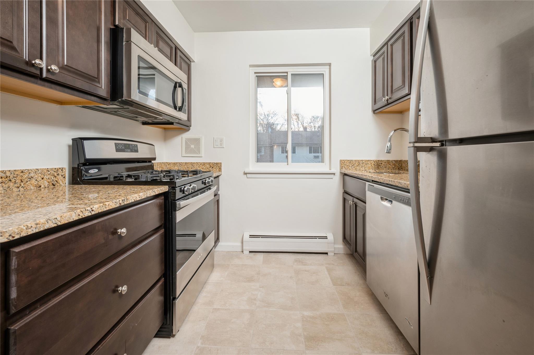 Kitchen featuring appliances with stainless steel finishes, light stone counters, dark brown cabinetry