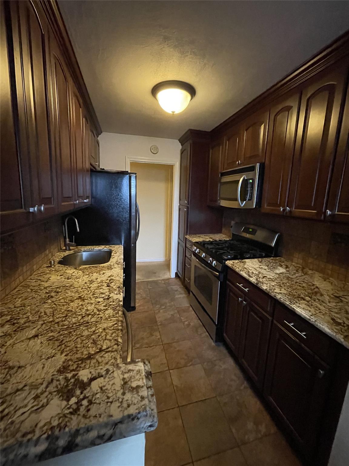 Kitchen featuring dark brown cabinetry, sink, appliances with stainless steel finishes, dark tile patterned flooring, and light stone countertops