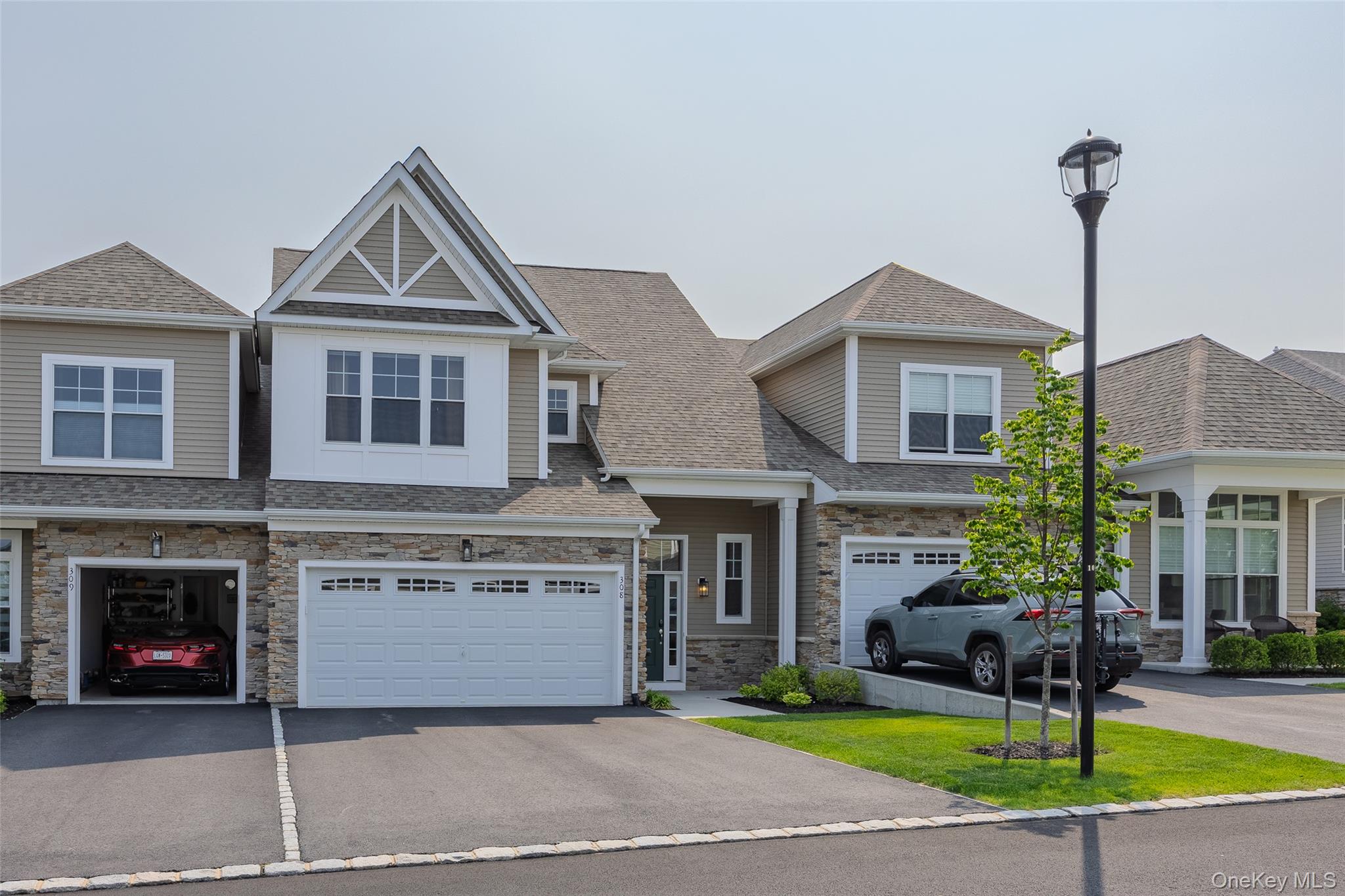 View of property featuring asphalt driveway, stone siding, a shingled roof, and an attached garage
