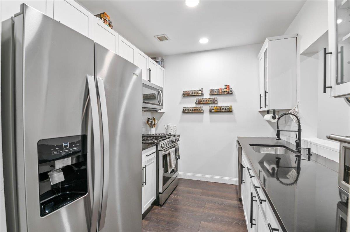 Kitchen with stainless steel appliances, white cabinetry, sink, and dark hardwood / wood-style floors