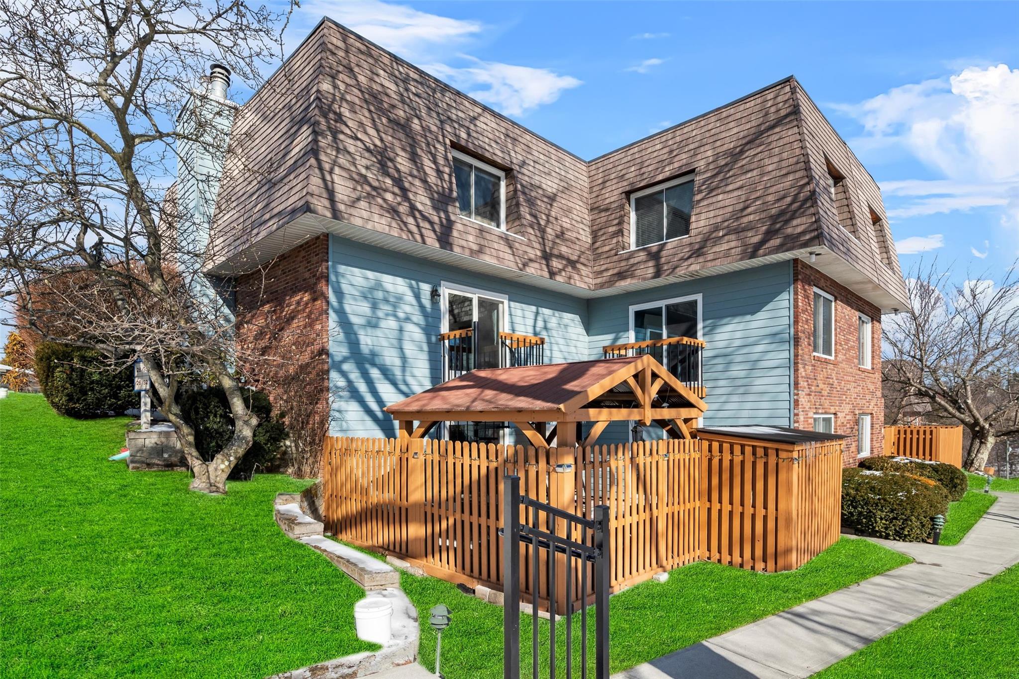 Back of house with brick siding, roof with shingles, a lawn, and mansard roof
