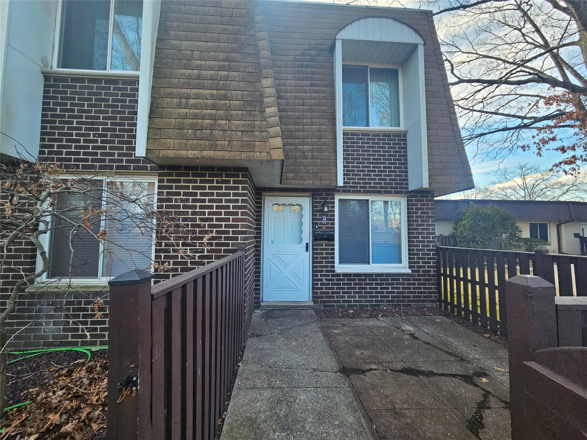 View of front of property featuring a shingled roof, fence, mansard roof, and brick siding