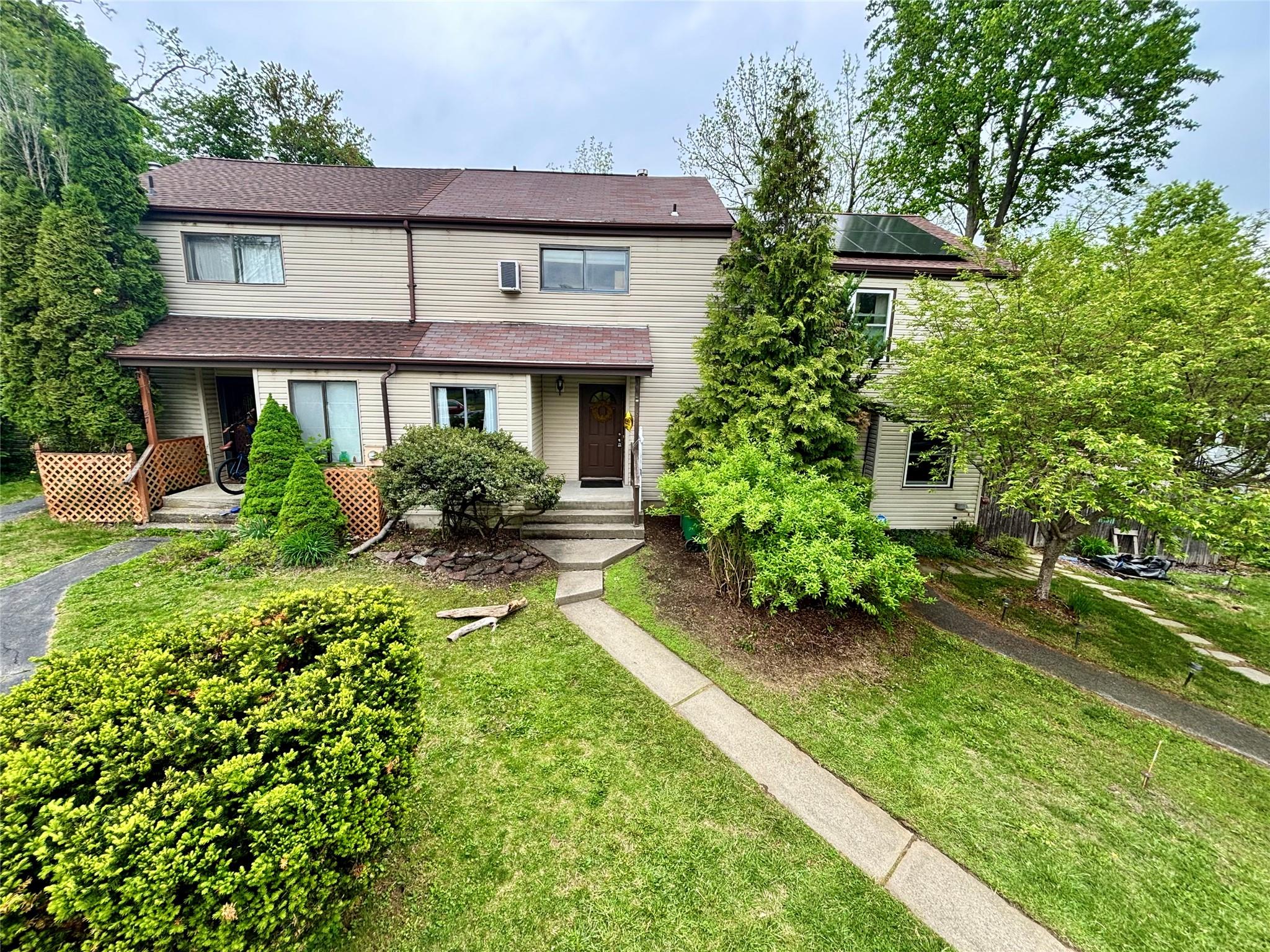 Multi unit property featuring covered porch, solar panels, and a front lawn