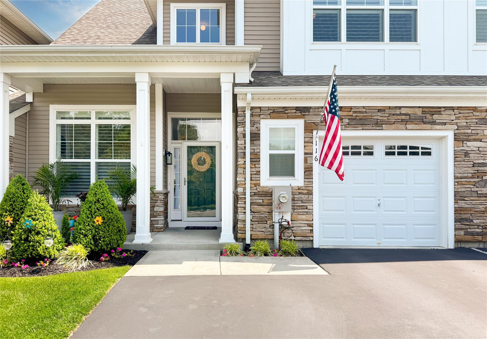 View of exterior entry with stone siding, an attached garage, a porch, and driveway