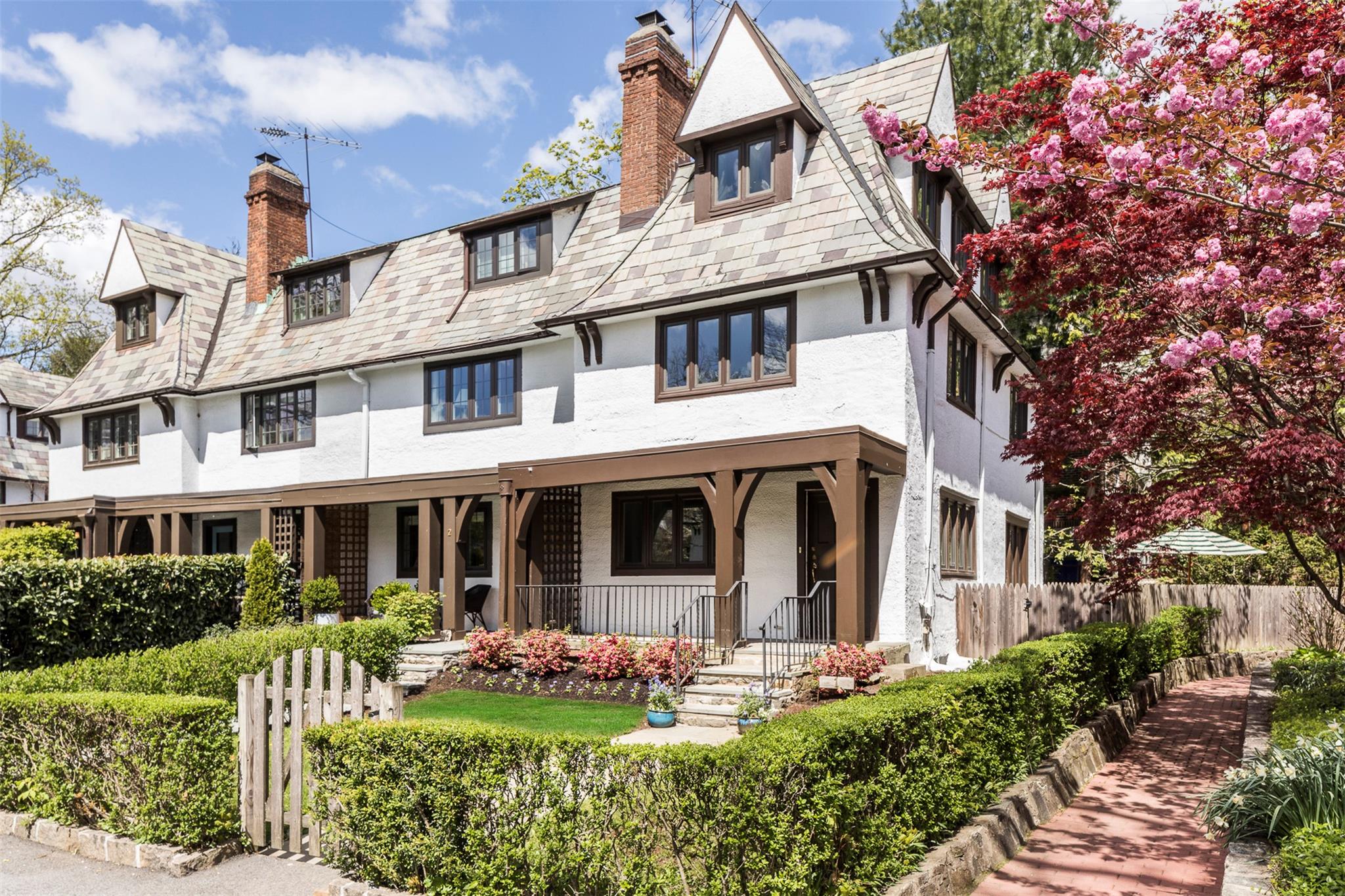 View of front of property featuring covered porch, fence, stucco siding, a chimney, and a high end roof