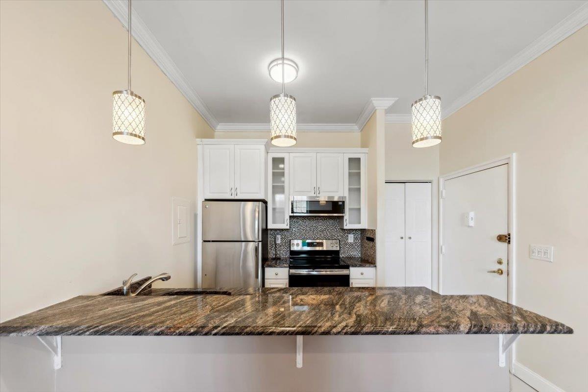 Kitchen with crown molding, stainless steel appliances, backsplash, a sink, and a peninsula