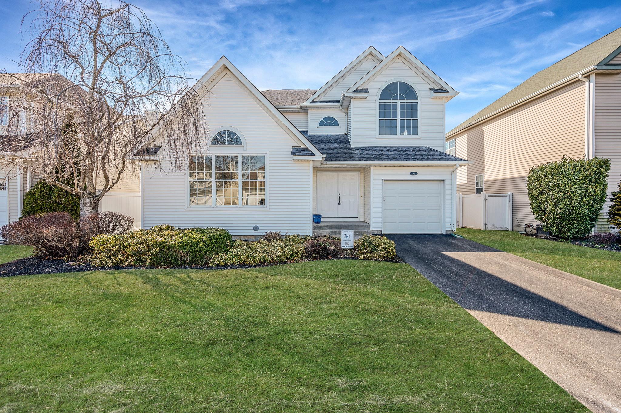 Traditional-style house with a garage, driveway, a front lawn, and roof with shingles