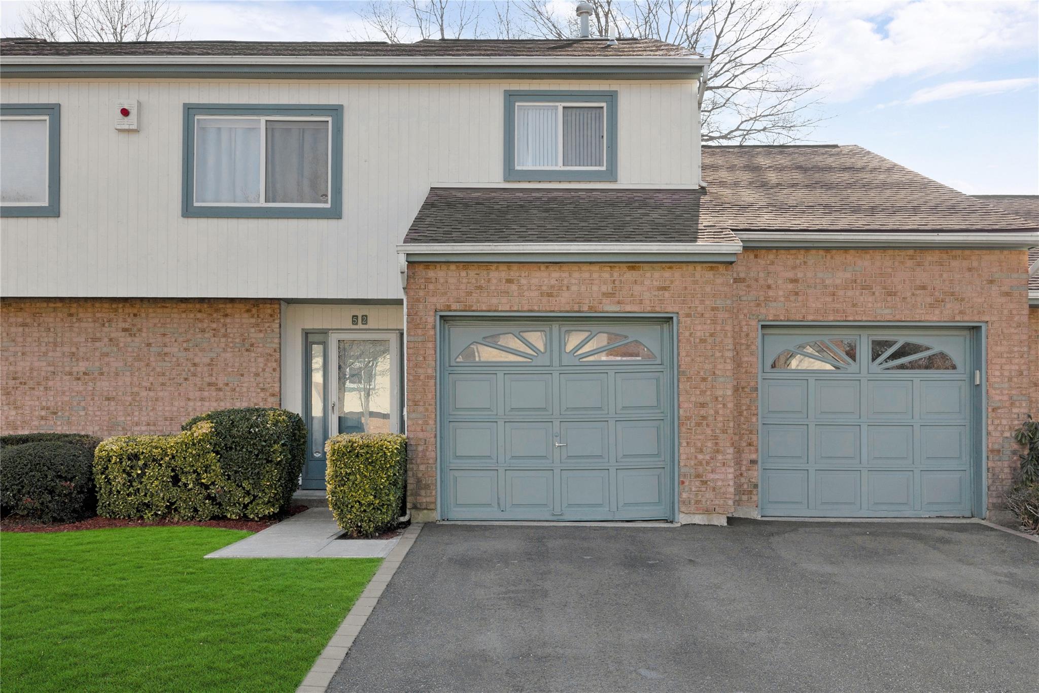 Multi unit property with a garage, brick siding, driveway, roof with shingles, and a front lawn