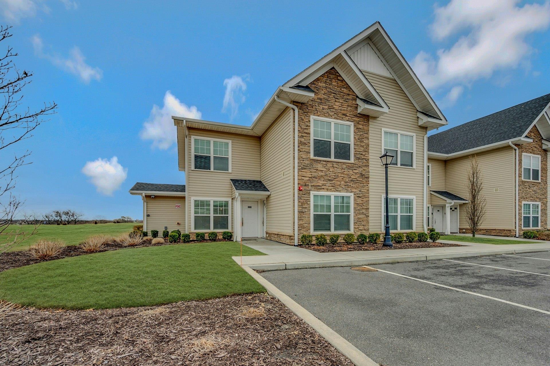 View of front facade featuring uncovered parking, stone siding, and a front lawn