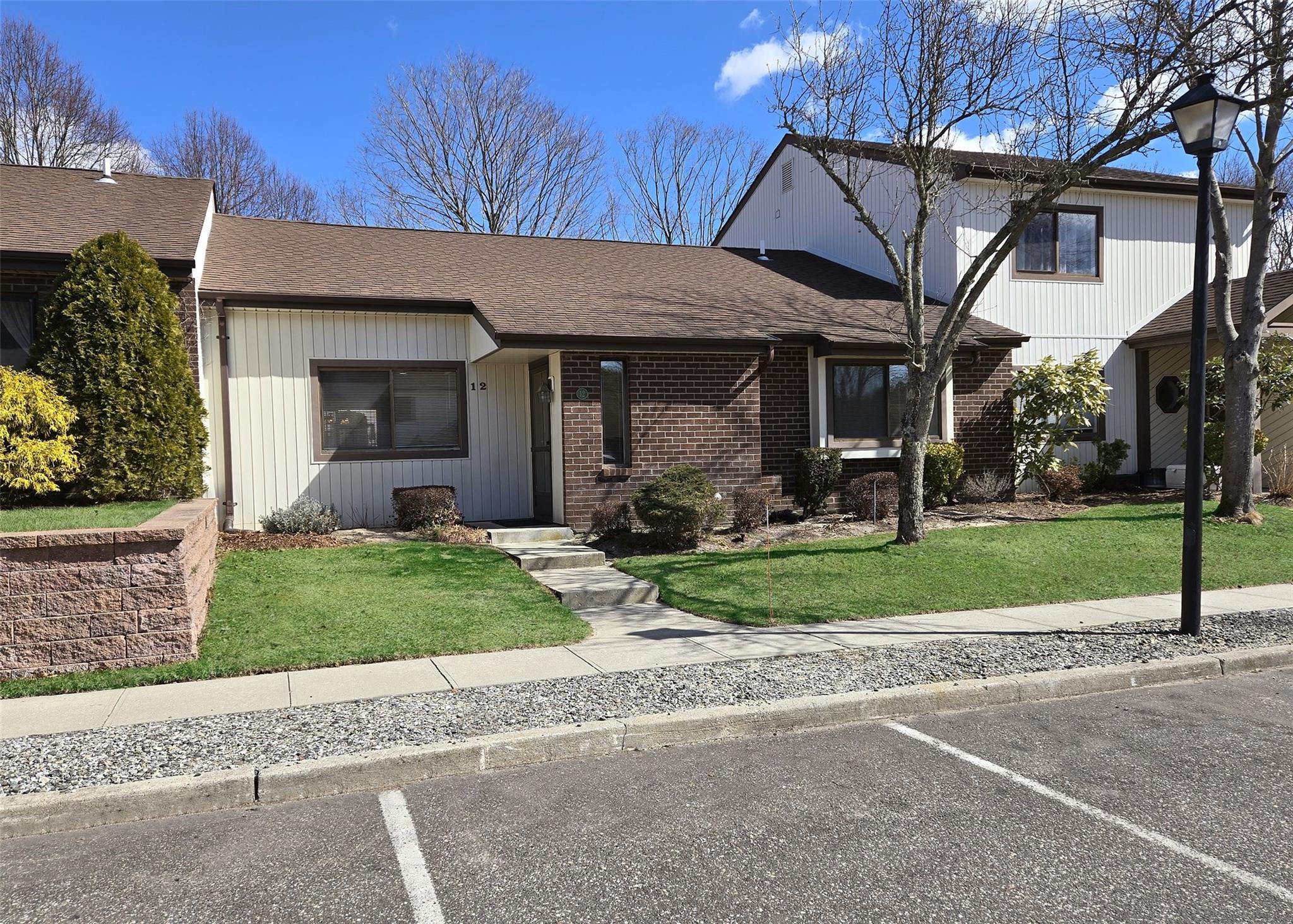 View of front facade with uncovered parking, brick siding, roof with shingles, and a front yard