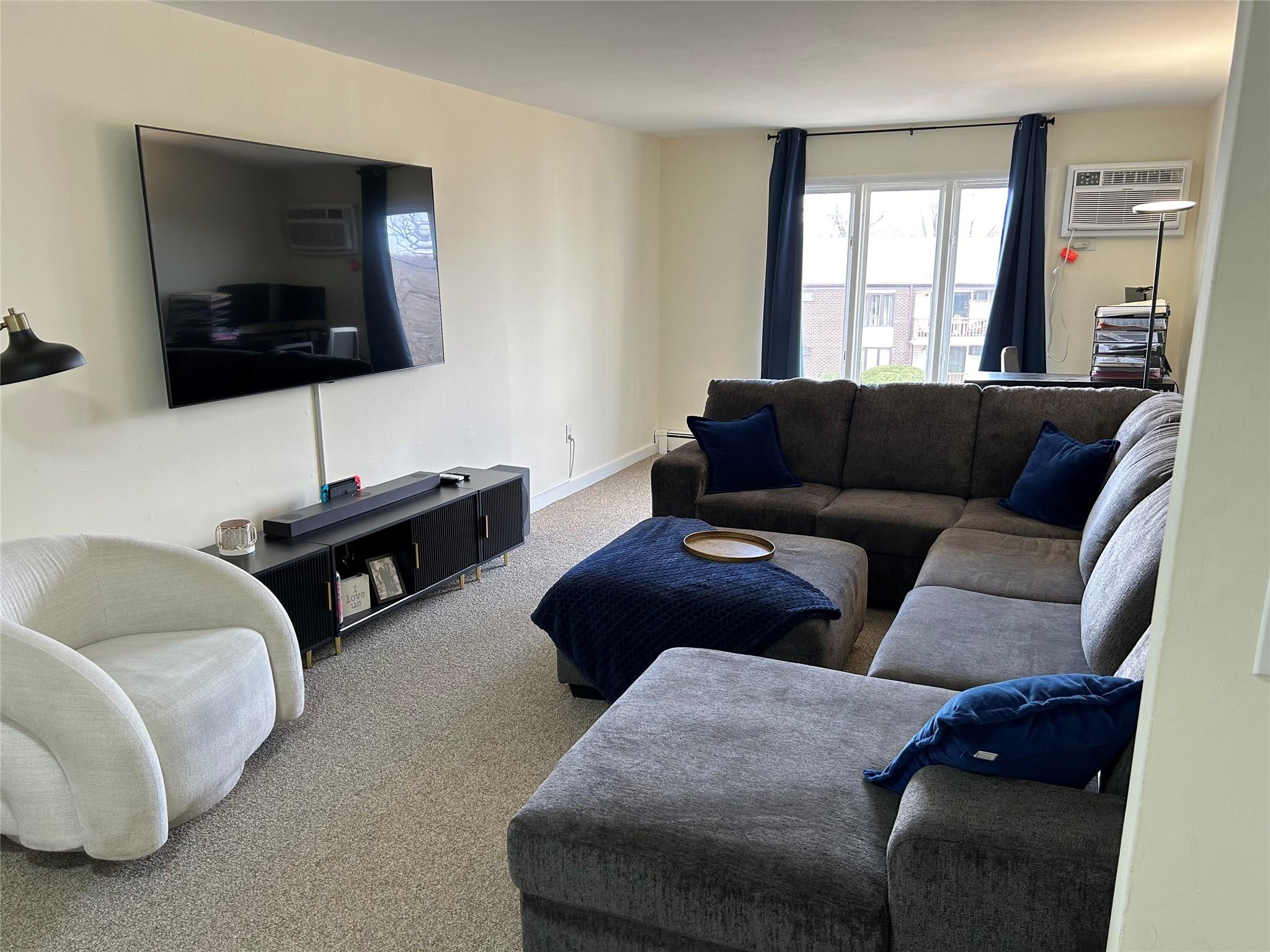 Plenty of room to entertain! Carpeted living area featuring baseboard heating, and a wall mounted air conditioner