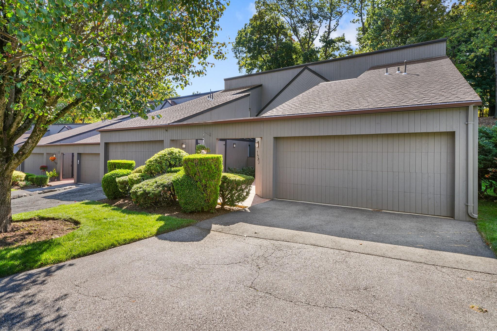 Mid-century home featuring an attached garage, driveway, and roof with shingles