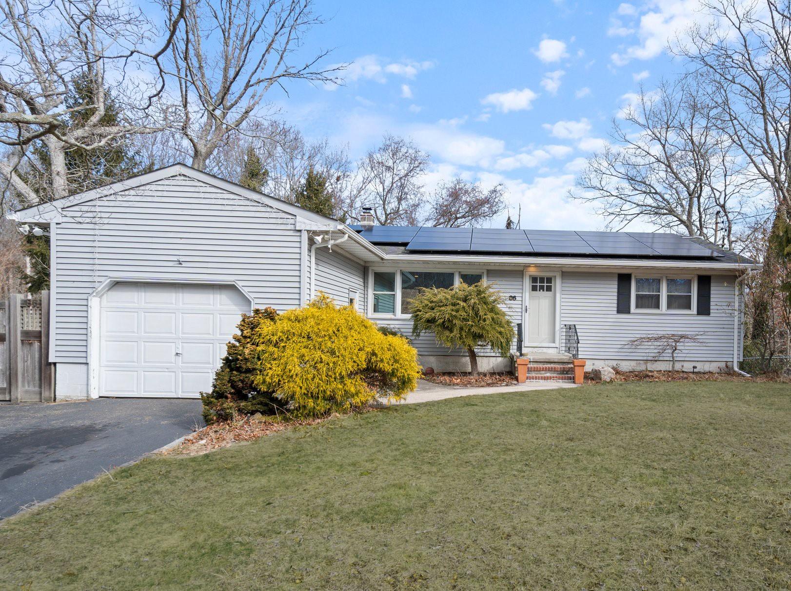 Single story home featuring driveway, a front lawn, an attached garage, solar panels, and a chimney