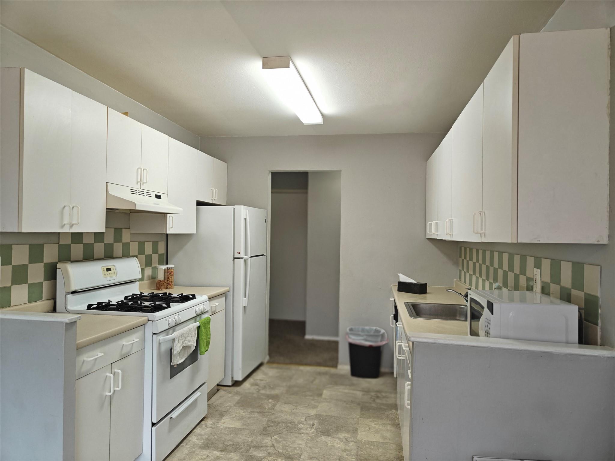 Kitchen with white appliances, a sink, light countertops, under cabinet range hood, and backsplash