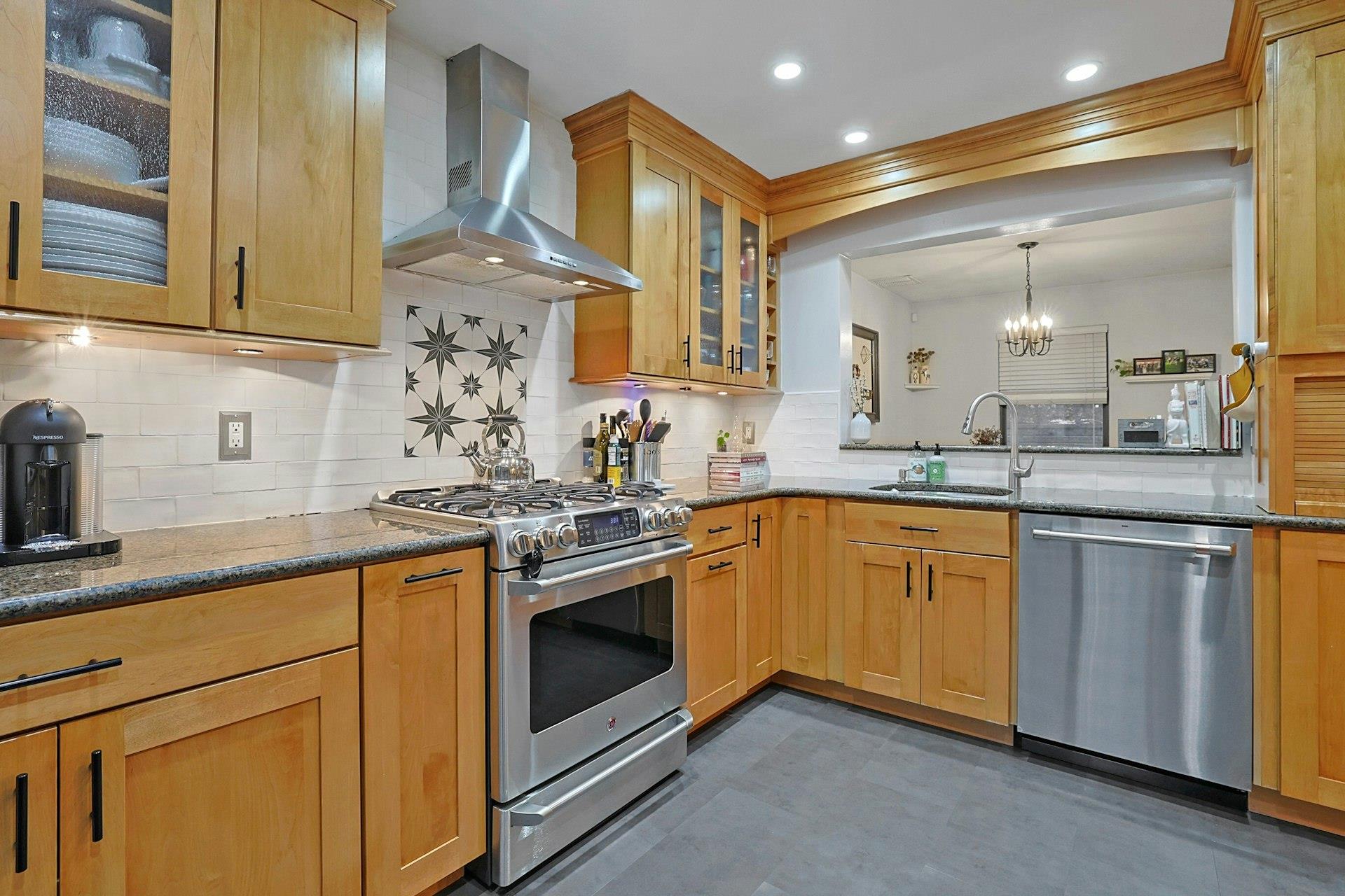 Kitchen with dark stone countertops, a sink, appliances with stainless steel finishes, wall chimney range hood, and a notable chandelier
