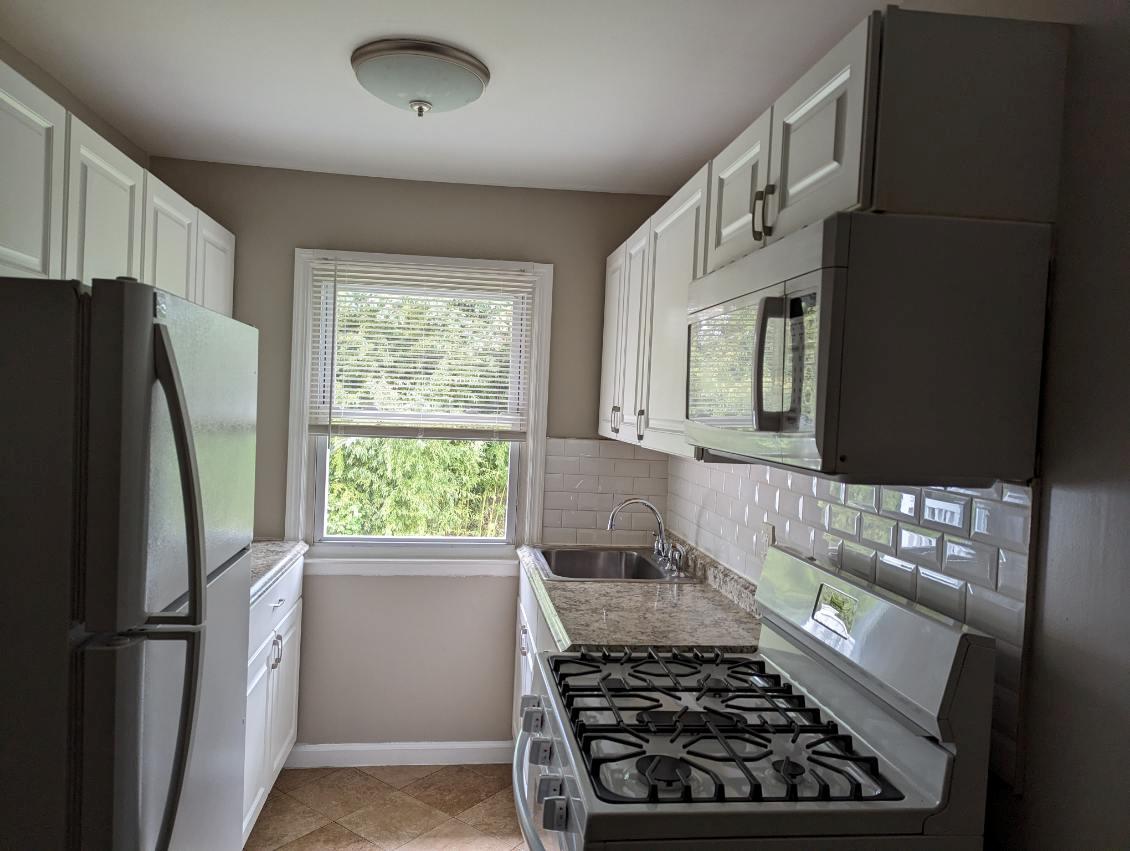 Kitchen featuring tasteful backsplash, stainless steel range with gas stovetop, freestanding refrigerator, white cabinets, and a sink