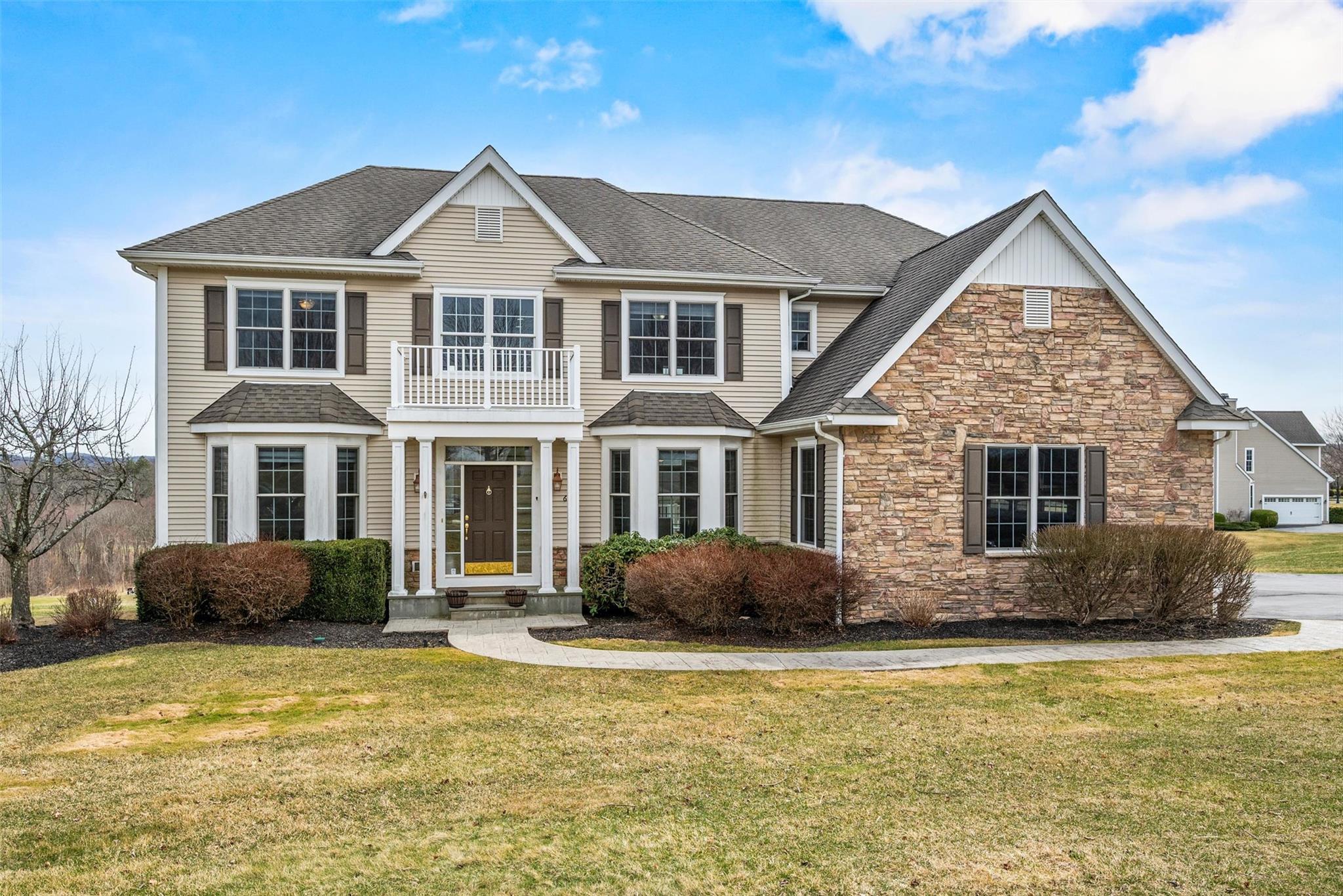 View of front facade featuring stone siding, a balcony, a shingled roof, and a front lawn