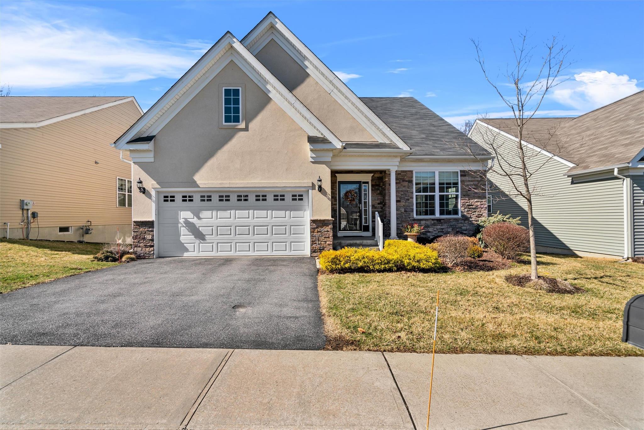 View of front of house with driveway, an attached garage, stucco siding, a front lawn, and stone siding