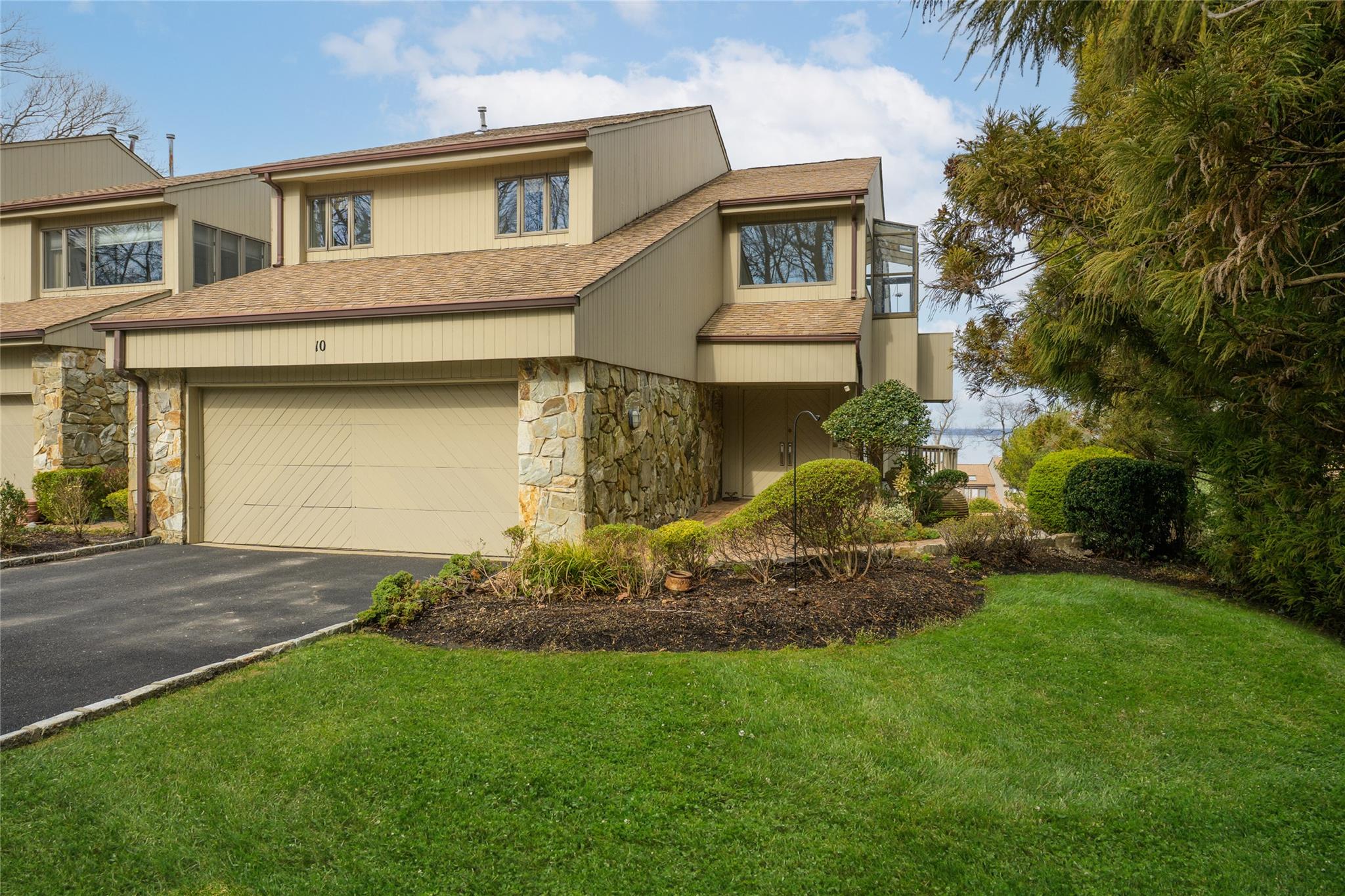 View of front of home featuring stone siding, a garage, a front yard, driveway, and a shingled roof