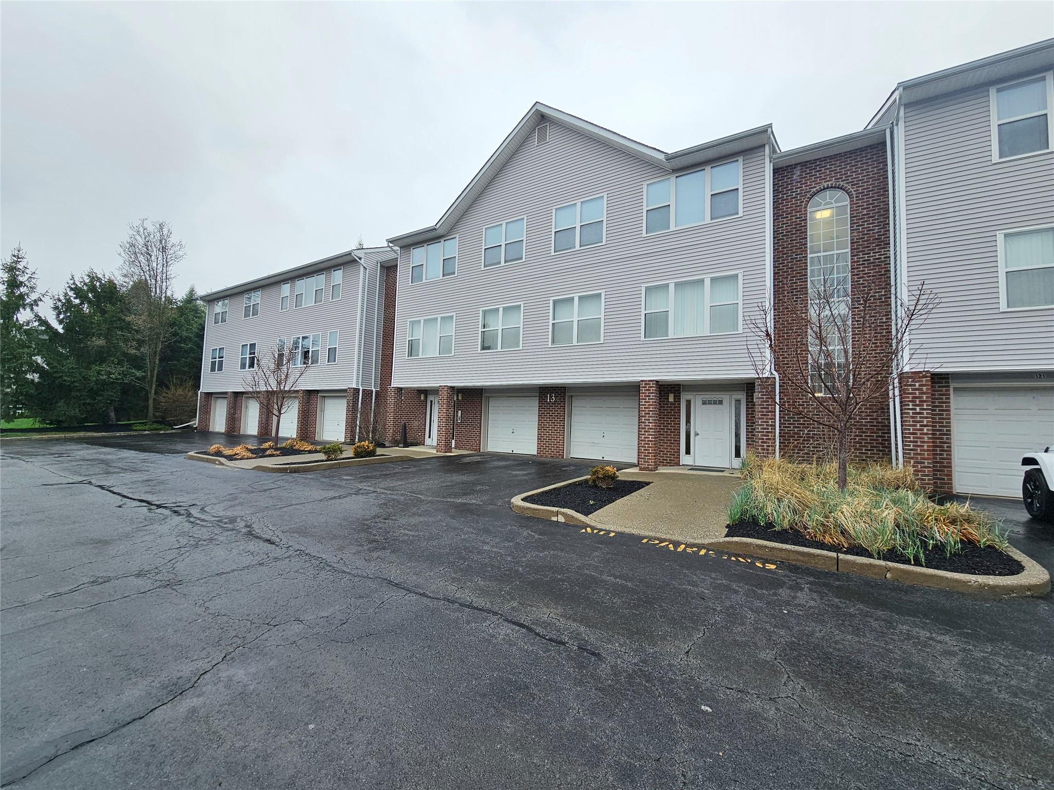 Multi unit property featuring an attached garage, driveway, a residential view, and brick siding