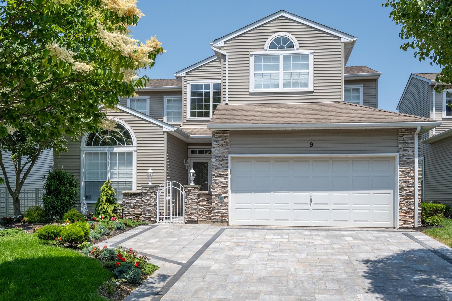View of front of home featuring decorative driveway, a shingled roof, an attached garage, and stone siding