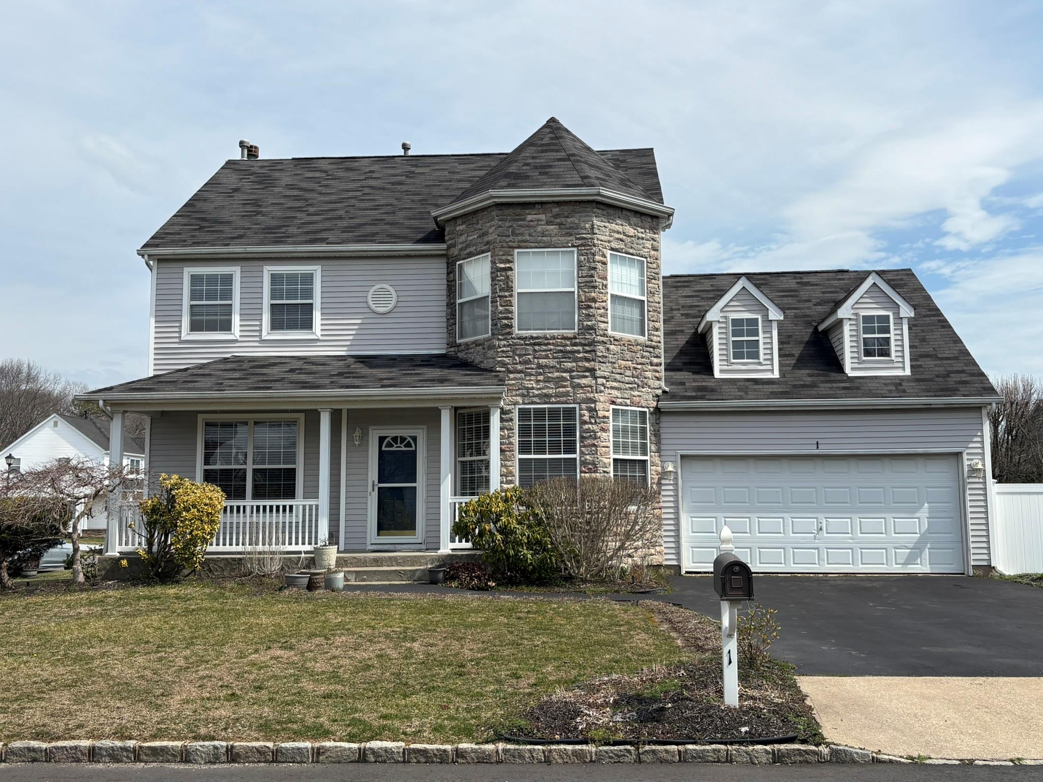 View of front of home with an attached garage, stone siding, aphalt driveway, a front lawn, and covered porch