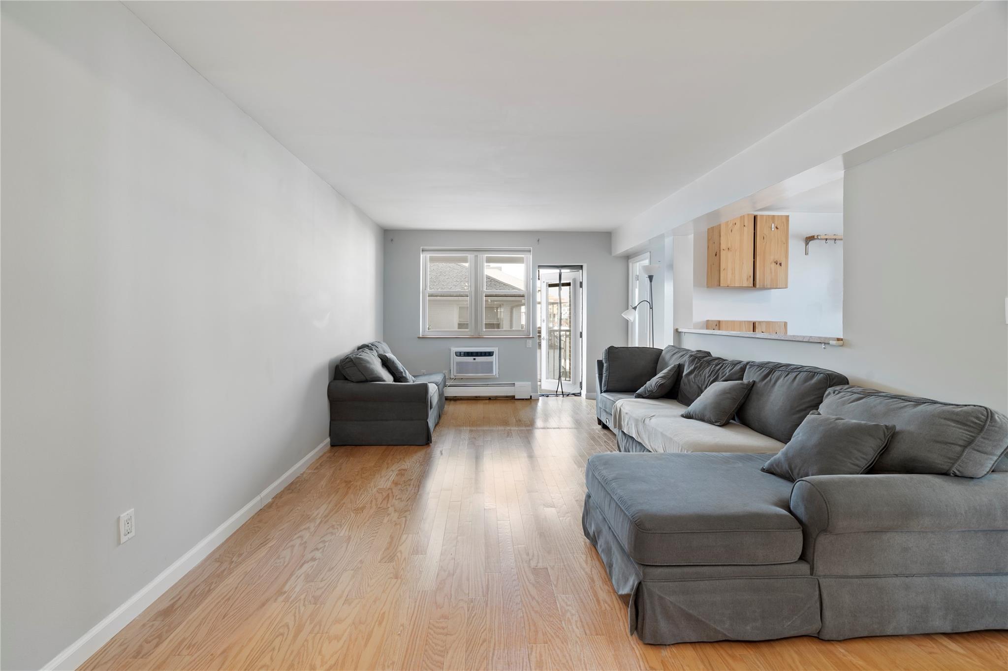 Living room featuring baseboards, an AC wall unit, and light wood-style floors