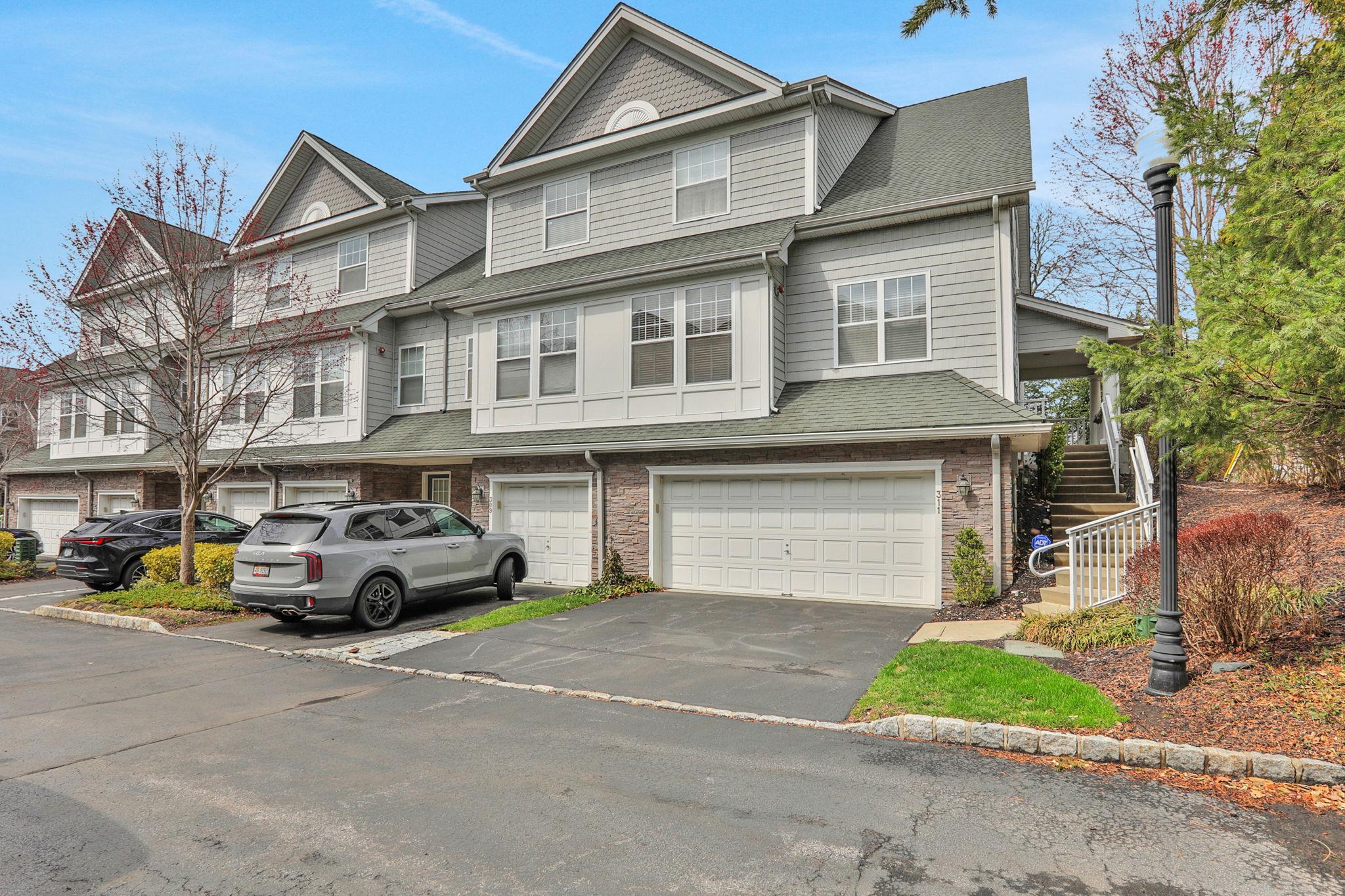View of property featuring driveway, an attached garage, stairs, and roof with shingles