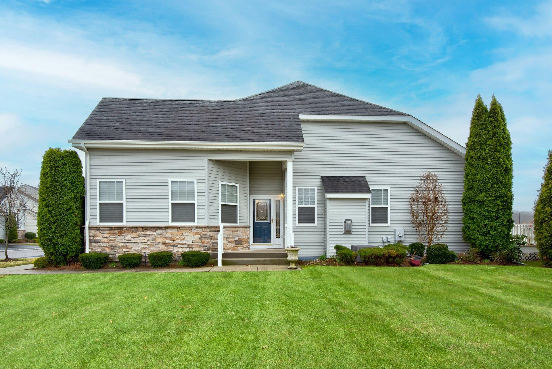 View of front facade with stone siding, a shingled roof, and a front lawn
