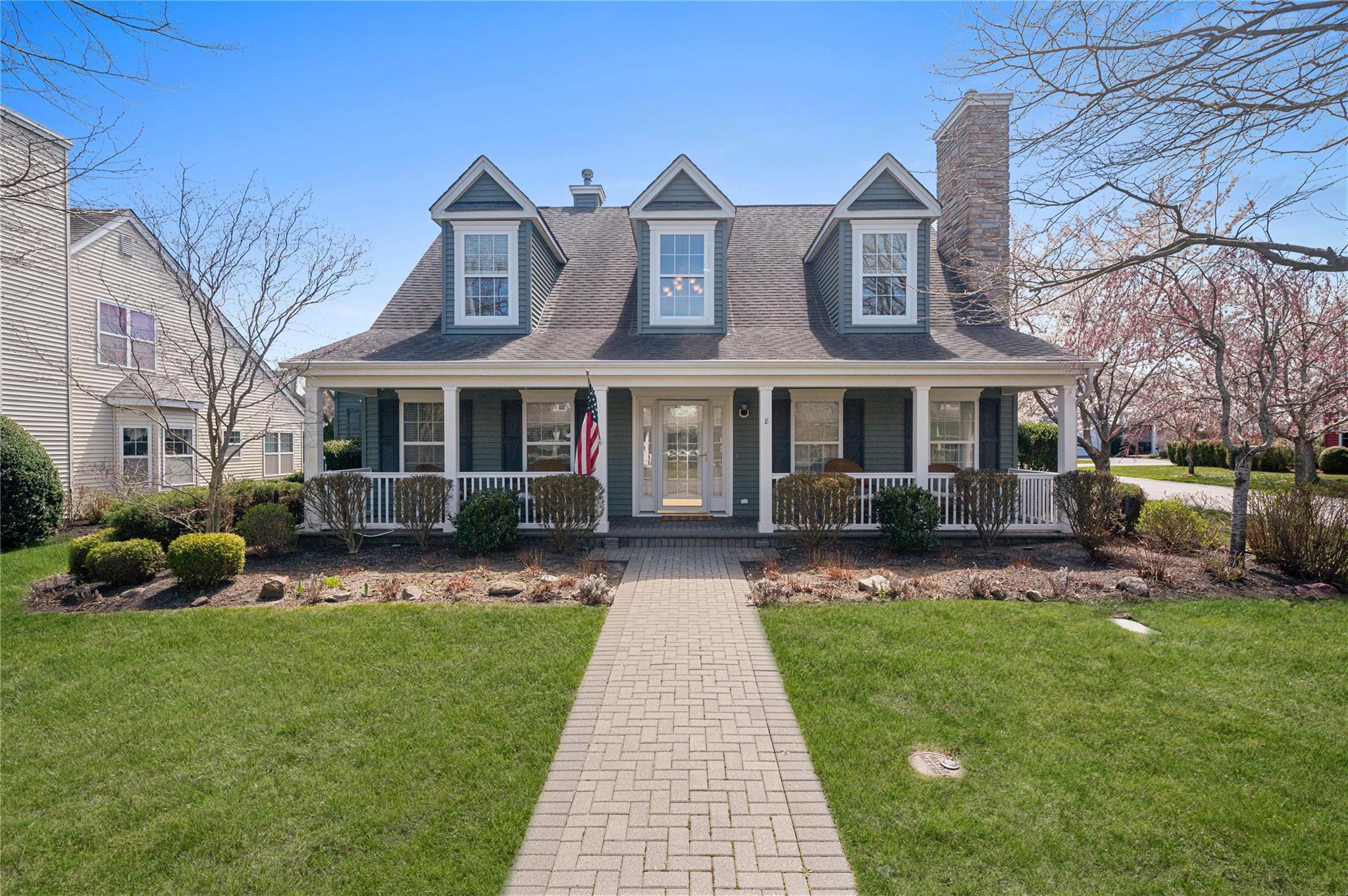 Cape cod-style house with roof with shingles, a front yard, a porch, and a chimney