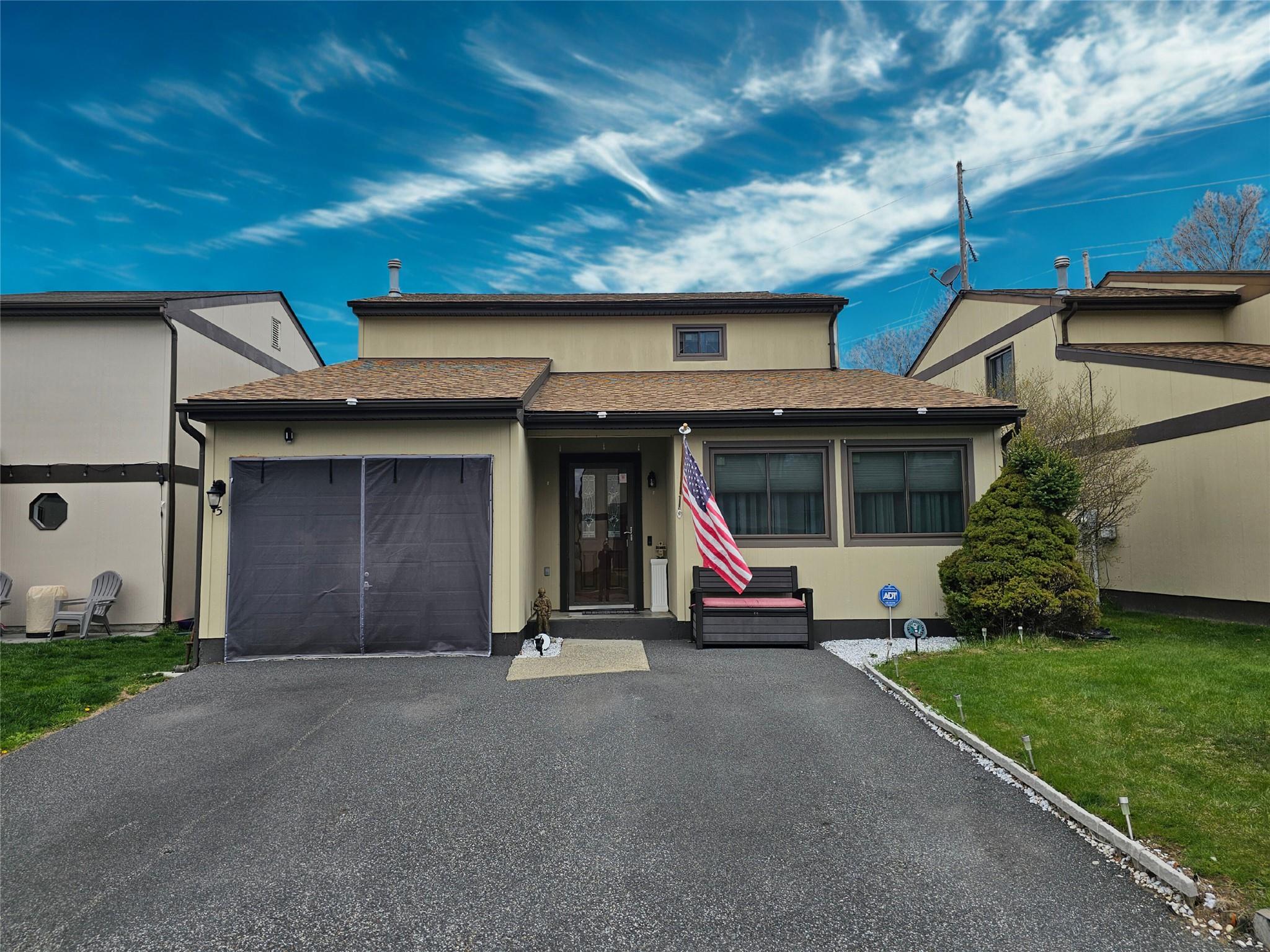 Townhome / multi-family property featuring an attached garage, a front lawn, aphalt driveway, and stucco siding