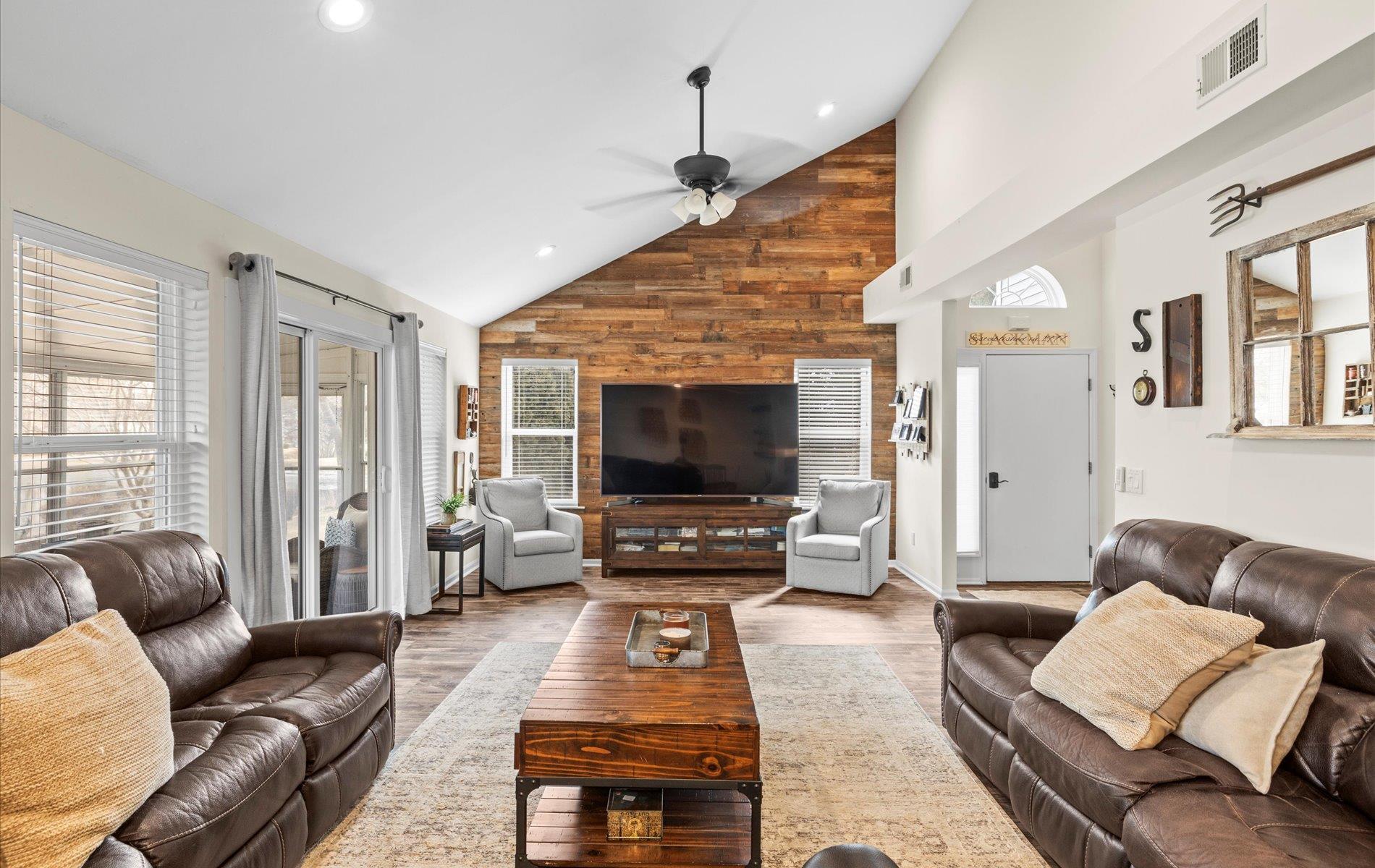 Living area featuring wood walls, wood finished floors, visible vents, high vaulted ceiling, and ceiling fan