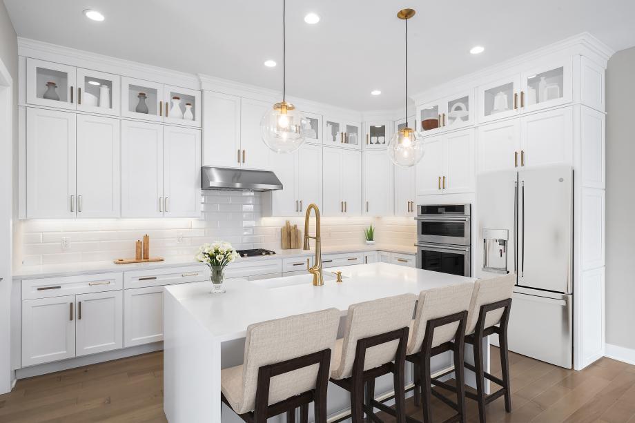 Kitchen featuring an island with sink, decorative backsplash, white fridge with ice dispenser, light countertops, and double oven