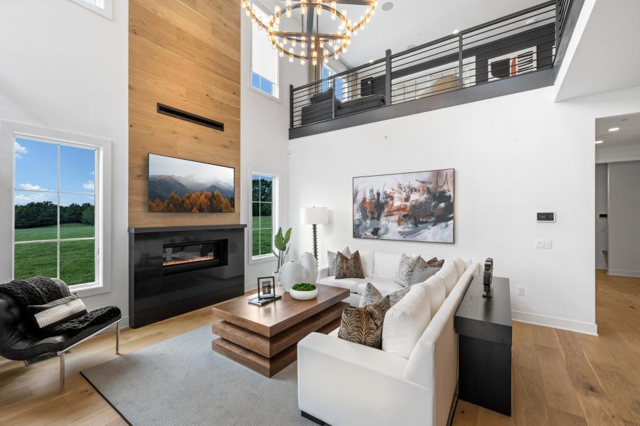 Living area with a towering ceiling, a notable chandelier, wood finished floors, and a glass covered fireplace