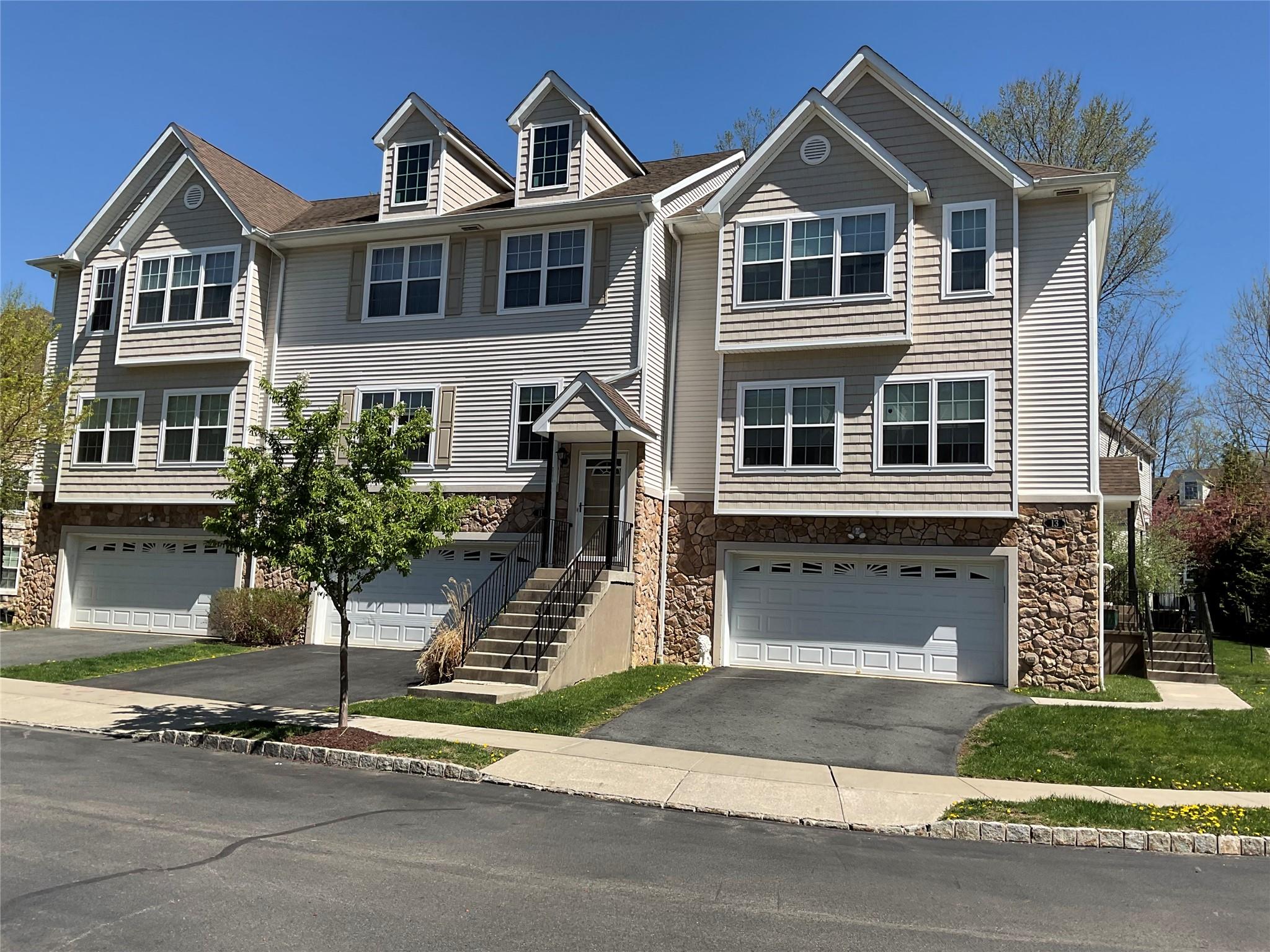 Townhome / multi-family property with an attached garage, driveway, and stone siding