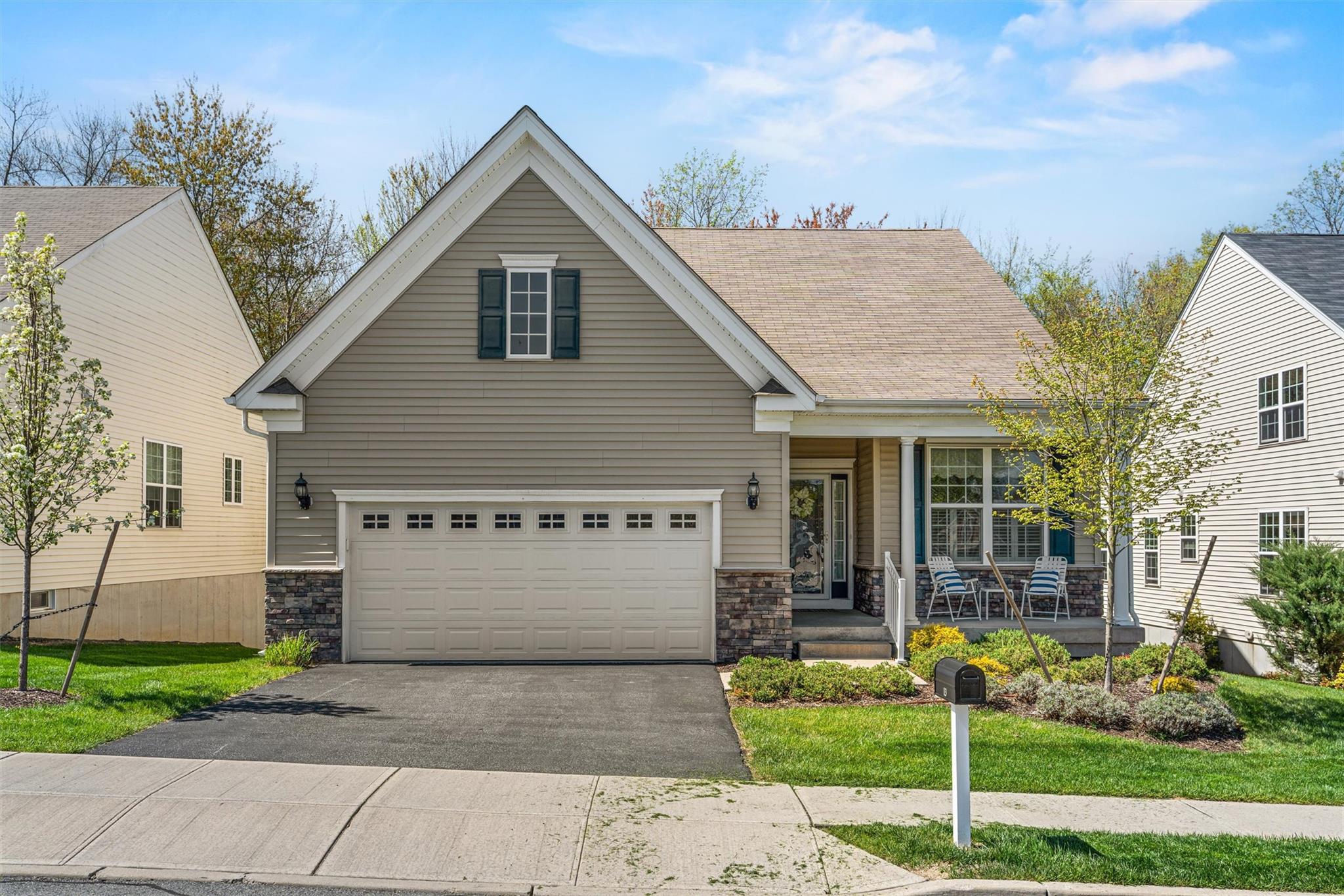 View of front of home featuring a front lawn, aphalt driveway, covered porch, stone siding, and an attached garage