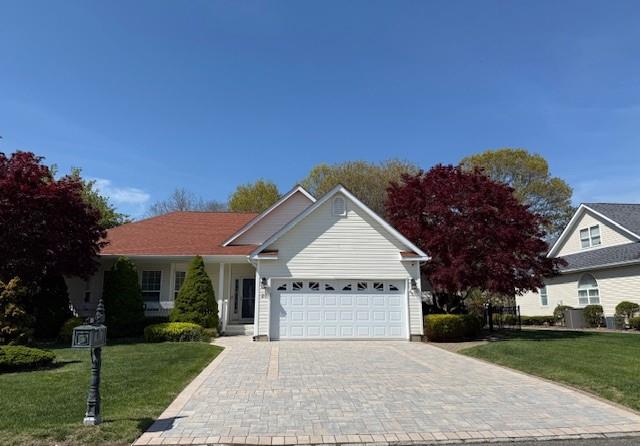 Single story home featuring an attached garage, decorative driveway, and a front lawn