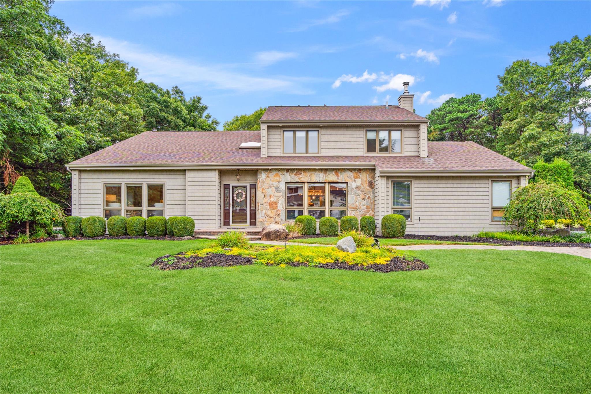 Traditional-style house with a chimney, stone siding, a shingled roof, and a front lawn