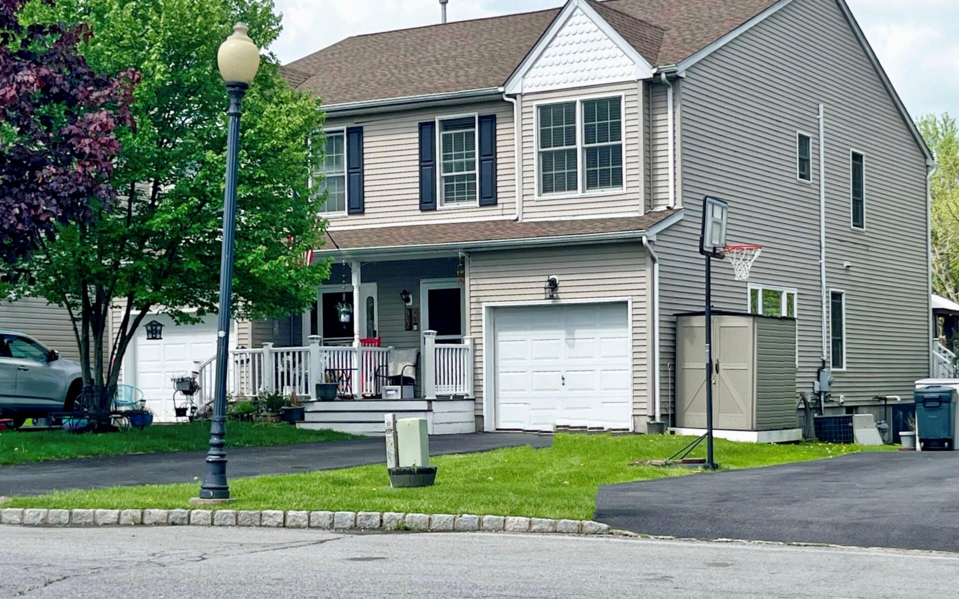 View of front of property with covered porch, a garage, driveway, a front yard, and roof with shingles