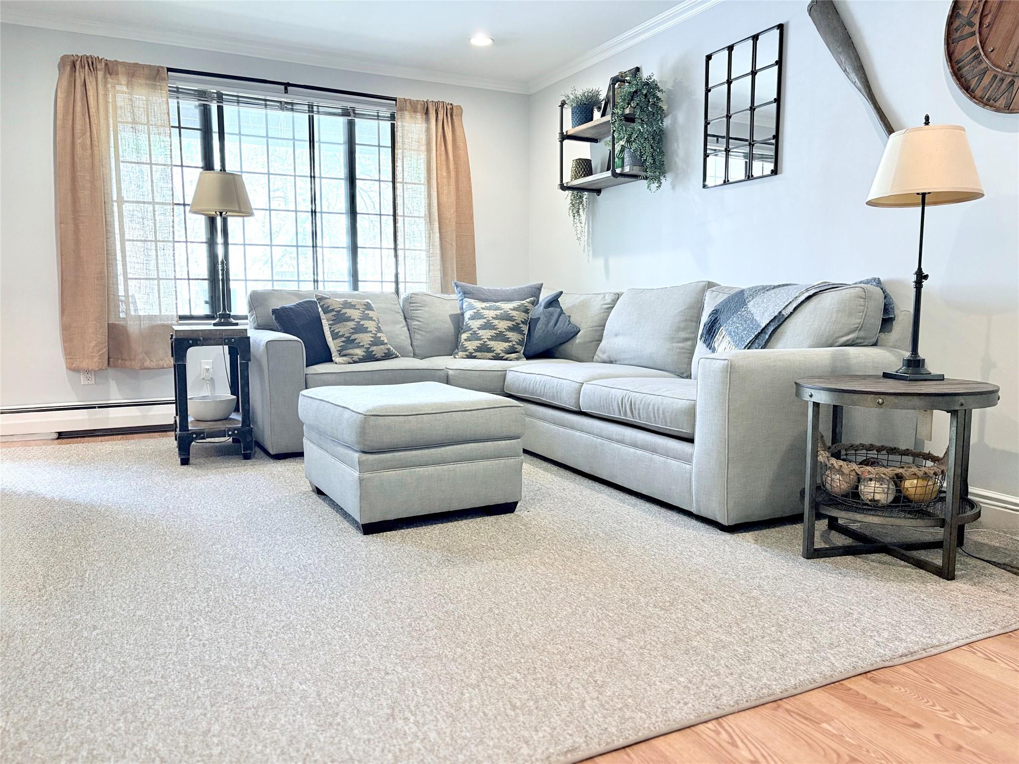 Living room with baseboard heating, ornamental molding, wood finished floors, baseboards, and recessed lighting