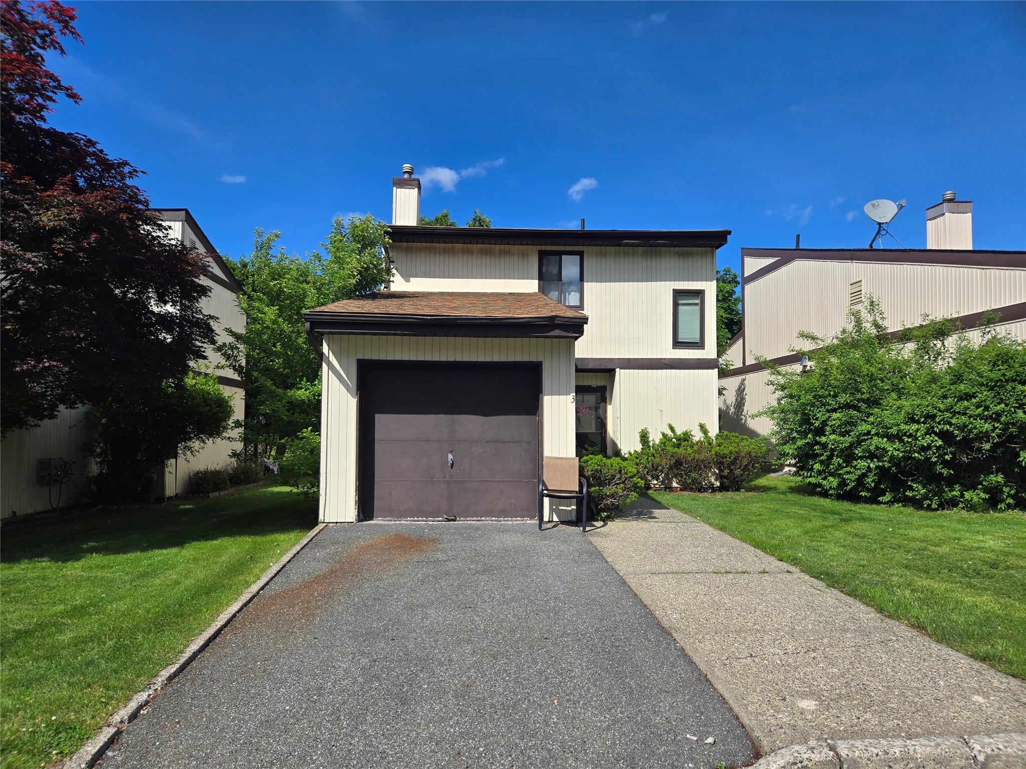 View of front of house featuring a chimney, a front lawn, driveway, and an attached garage