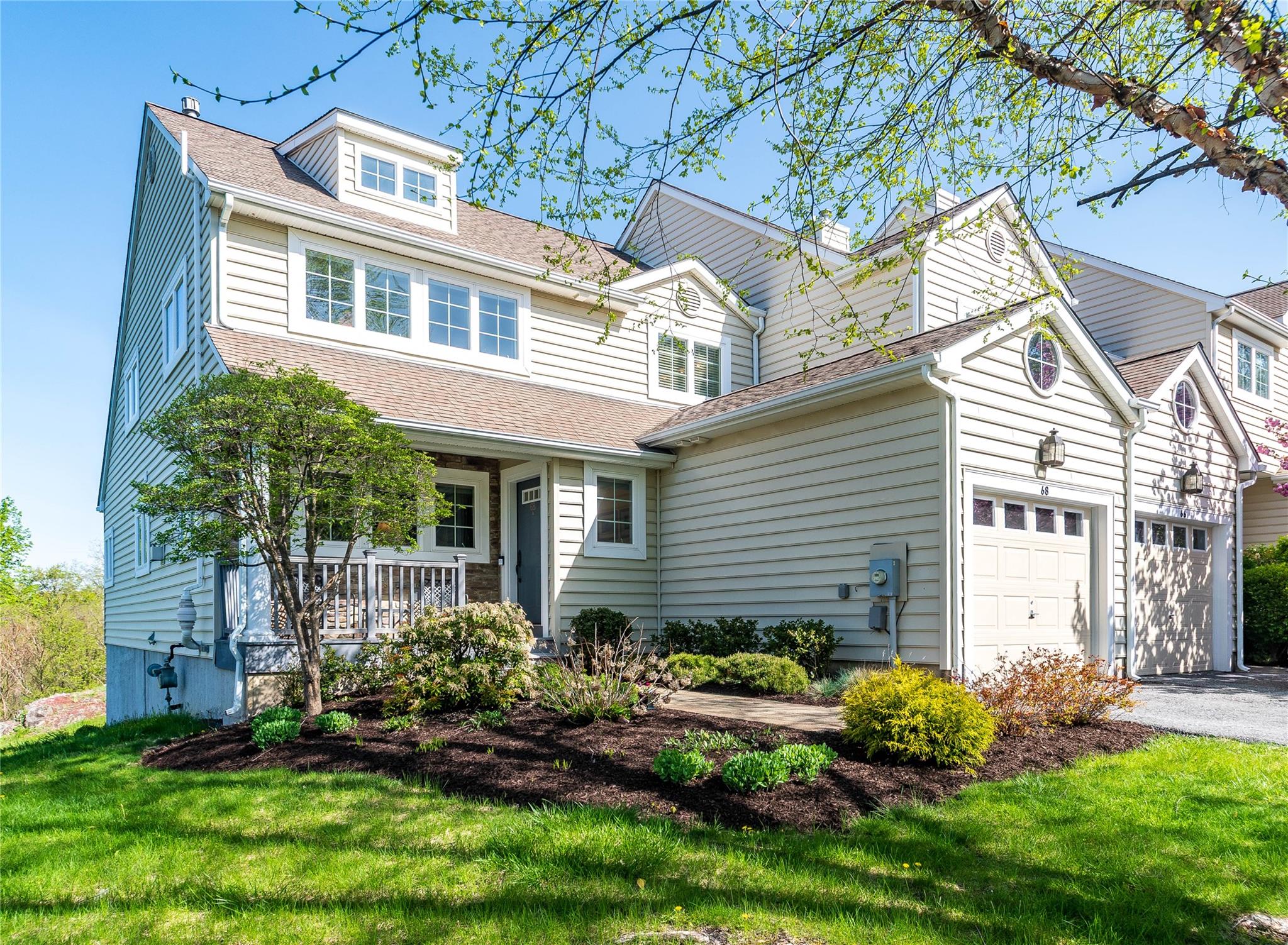 Townhouse-style home with a porch, a front lawn, asphalt driveway, an attached garage, and a shingled roof