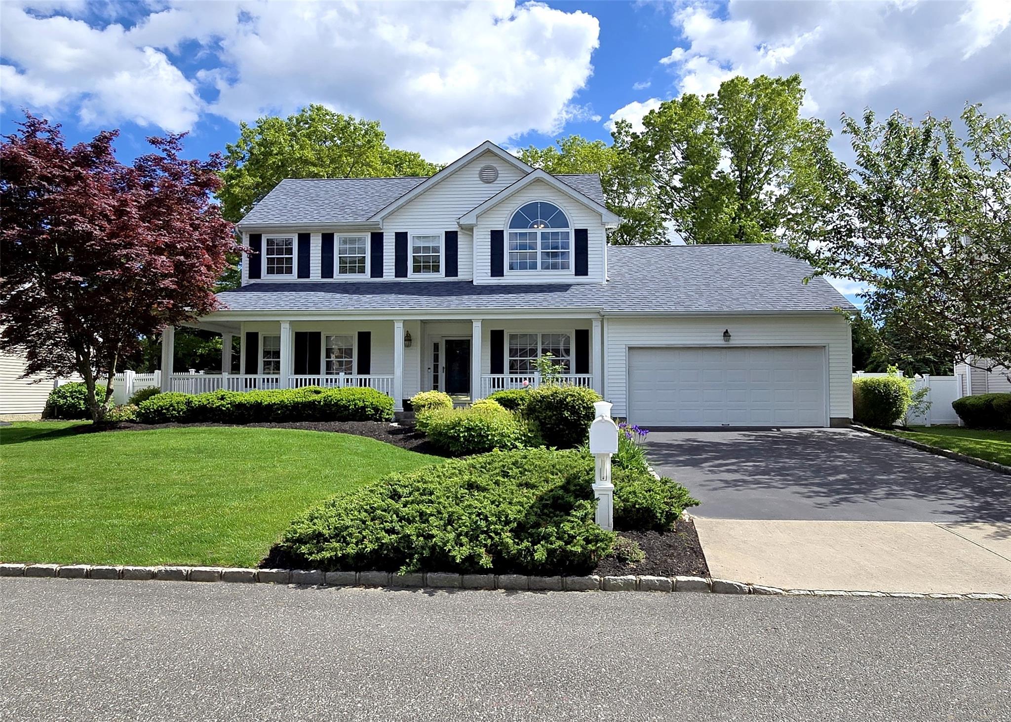 Colonial-style house featuring driveway, covered porch, an attached garage, a front yard, and a shingled roof