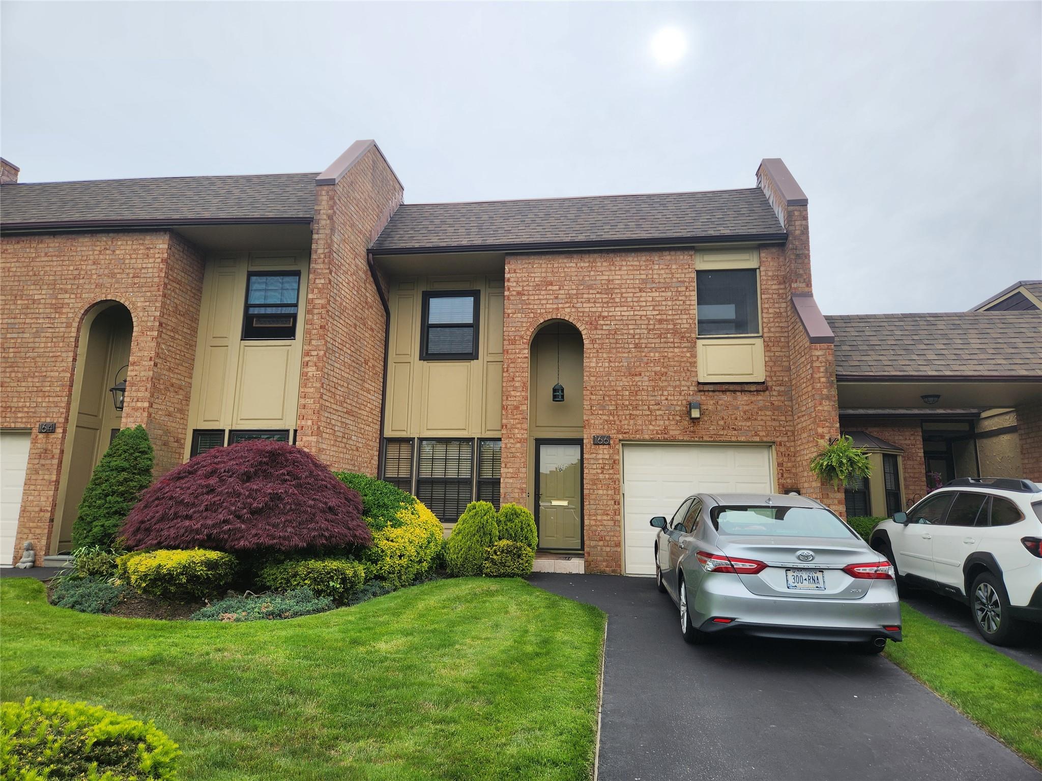 Multi unit property with brick siding, roof with shingles, driveway, a garage, and a front yard